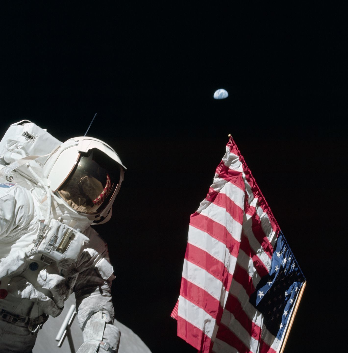 astronaut harrison schmitt beside the american flag on the lunar surface with earth visible in the black sky above