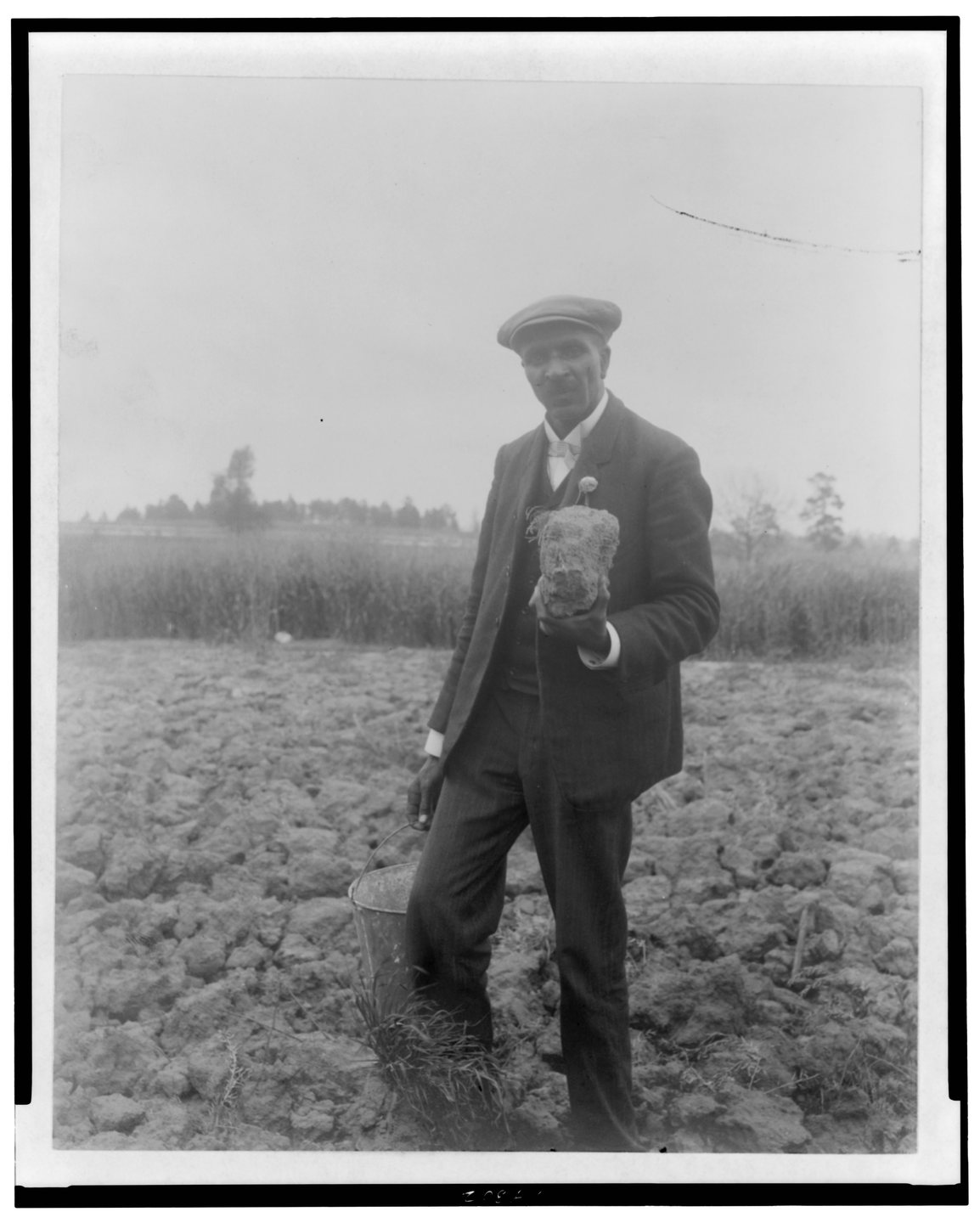 George Washington Carver standing in a field holding soil, Tuskegee, 1906